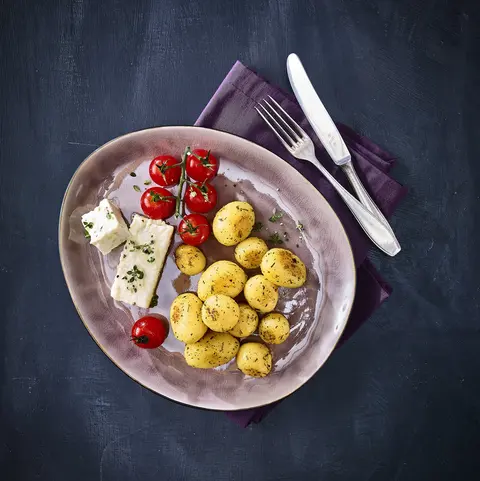 Drei knusprige Kartoffel-Reibekuchen auf einem weißen Teller, serviert mit einem fruchtigen Glühwein-Apfelmus. Dekoriert mit einer frischen Orangenscheibe und Minzblättern. Im Hintergrund Gewürze wie Zimtstangen, Sternanis und Orangenscheiben sowie eine Tasse dampfender Glühwein mit einer Zimtstange. Das Besteck liegt auf einer olivgrünen Stoffserviette, arrangiert auf einem dunklen Untergrund.